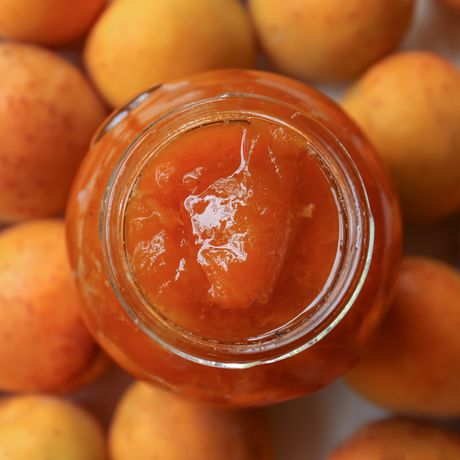 Vaso aperto di composta biologica di albicocche con frutta fresca sullo sfondo.