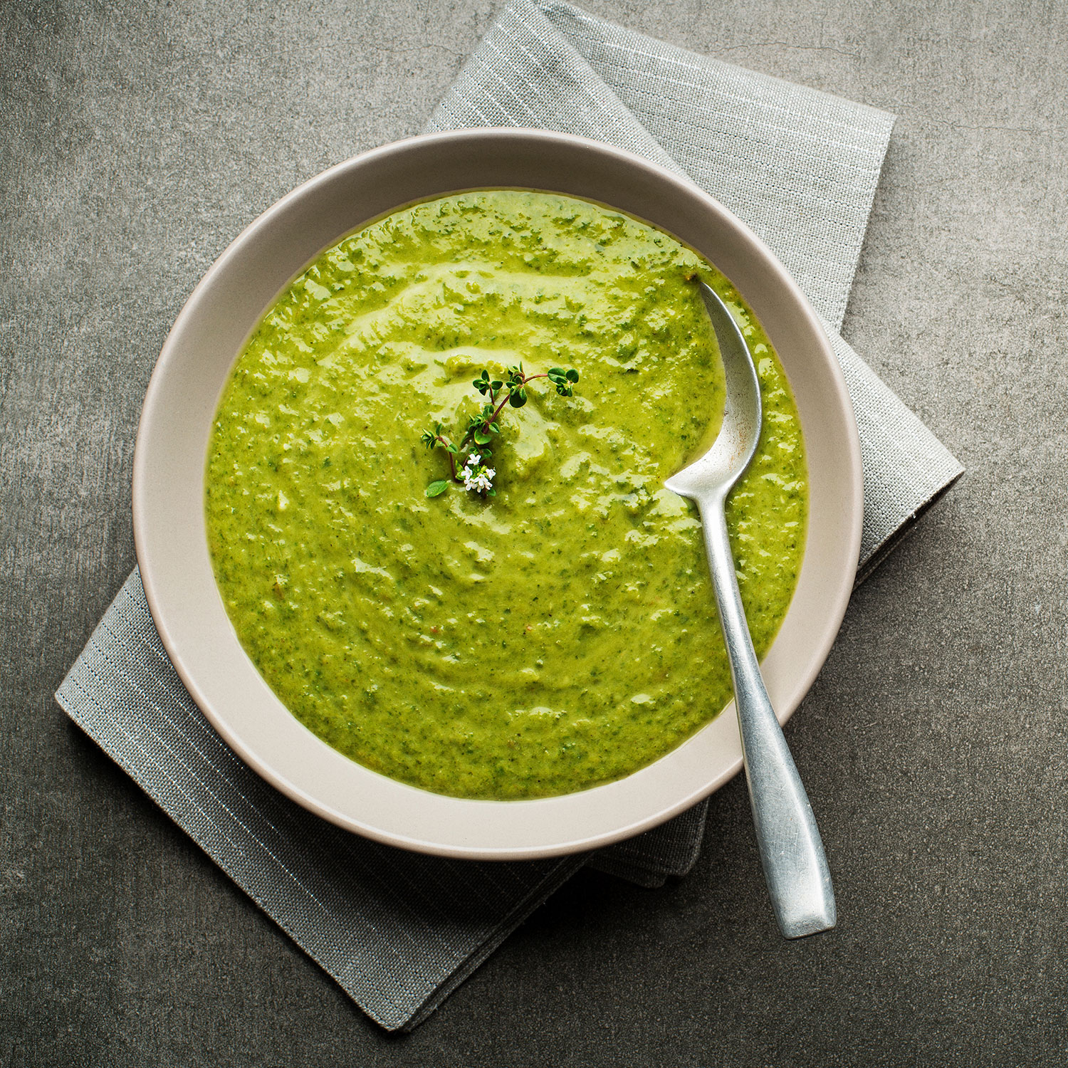 Vellutata verde cremosa servita in ciotola beige con cucchiaio