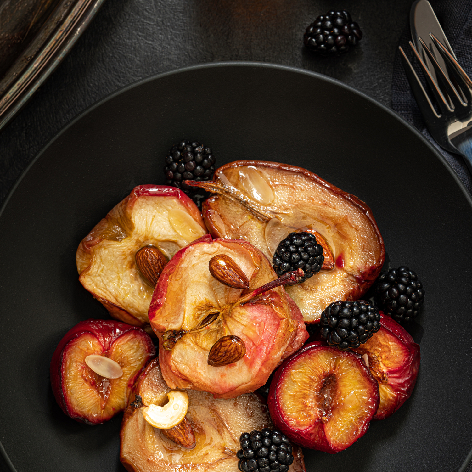 Pere Madernassa caramellate con more fresche e mandorle in ciotola nera.