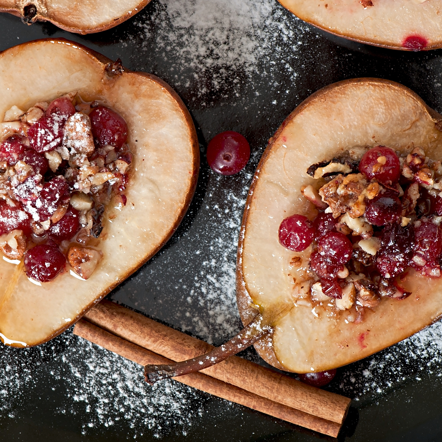 Pere Madernassa al forno con noci, frutti rossi e cannella su piatto scuro.